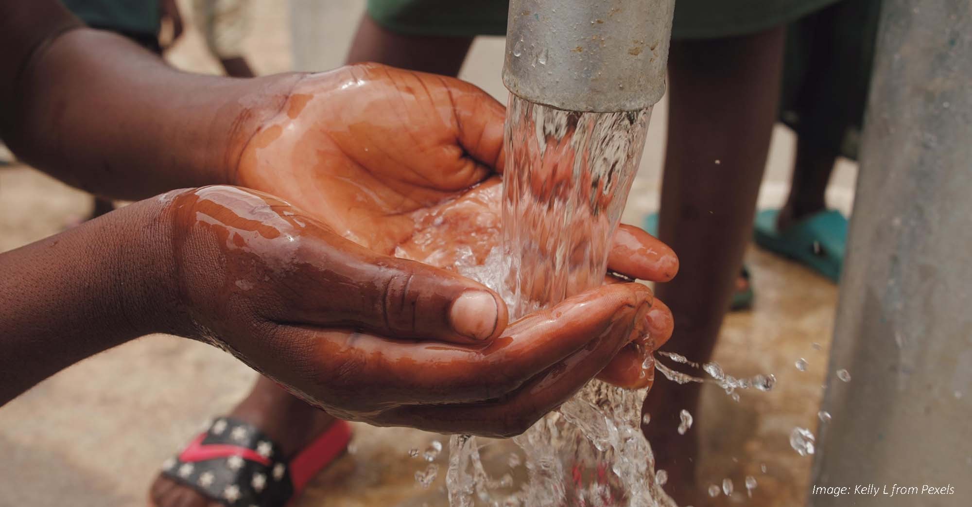 Close-up of a child's hands cupped together under running water from an outdoor pipe